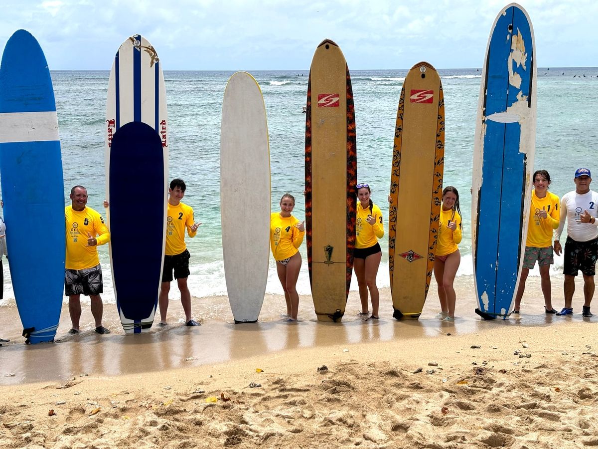 SFC surf lesson students standing with longboards along the Waikīkī shoreline
