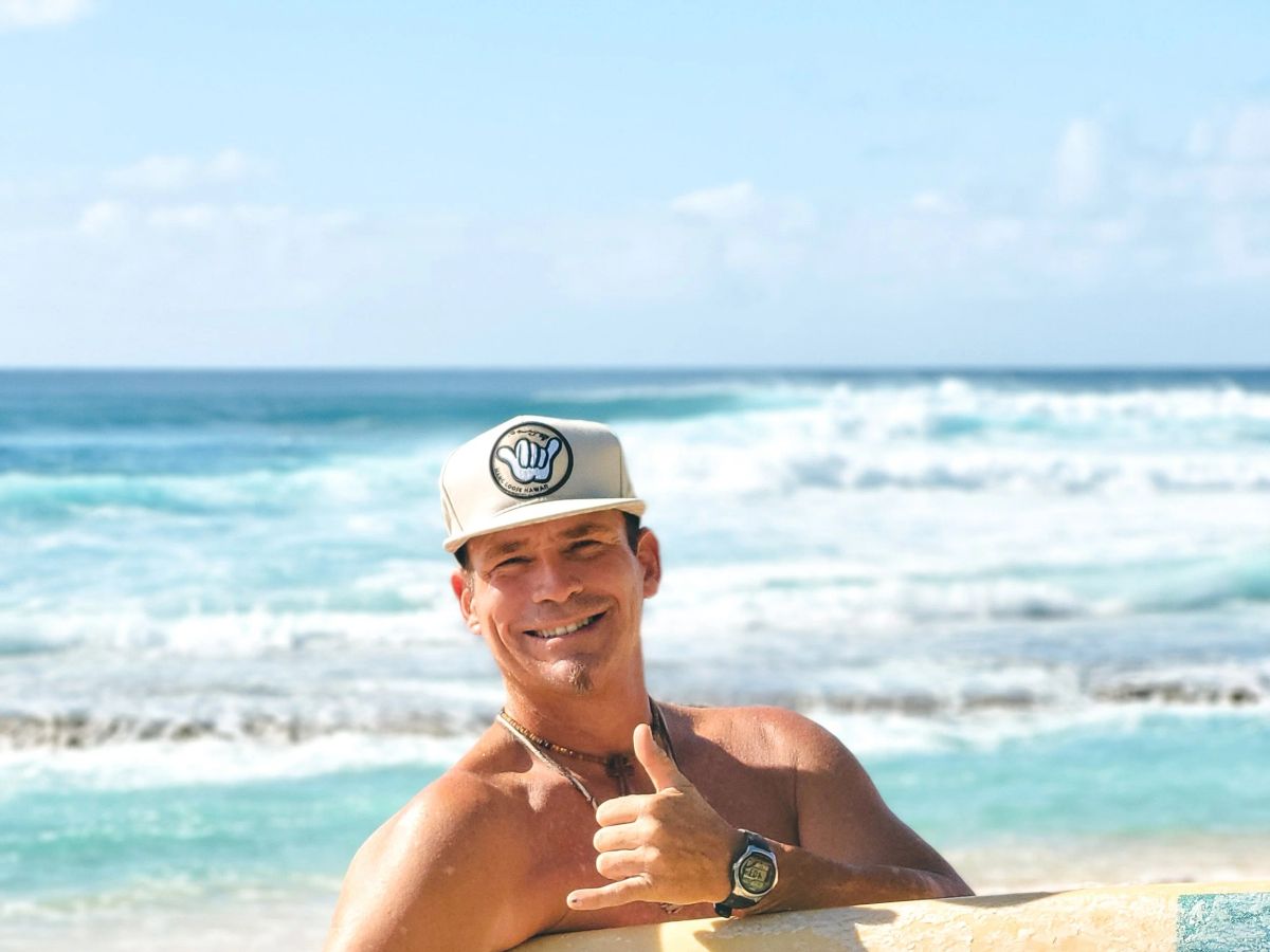 Uncle Savage smiling with an SFC surfboard at the Waikīkī shoreline