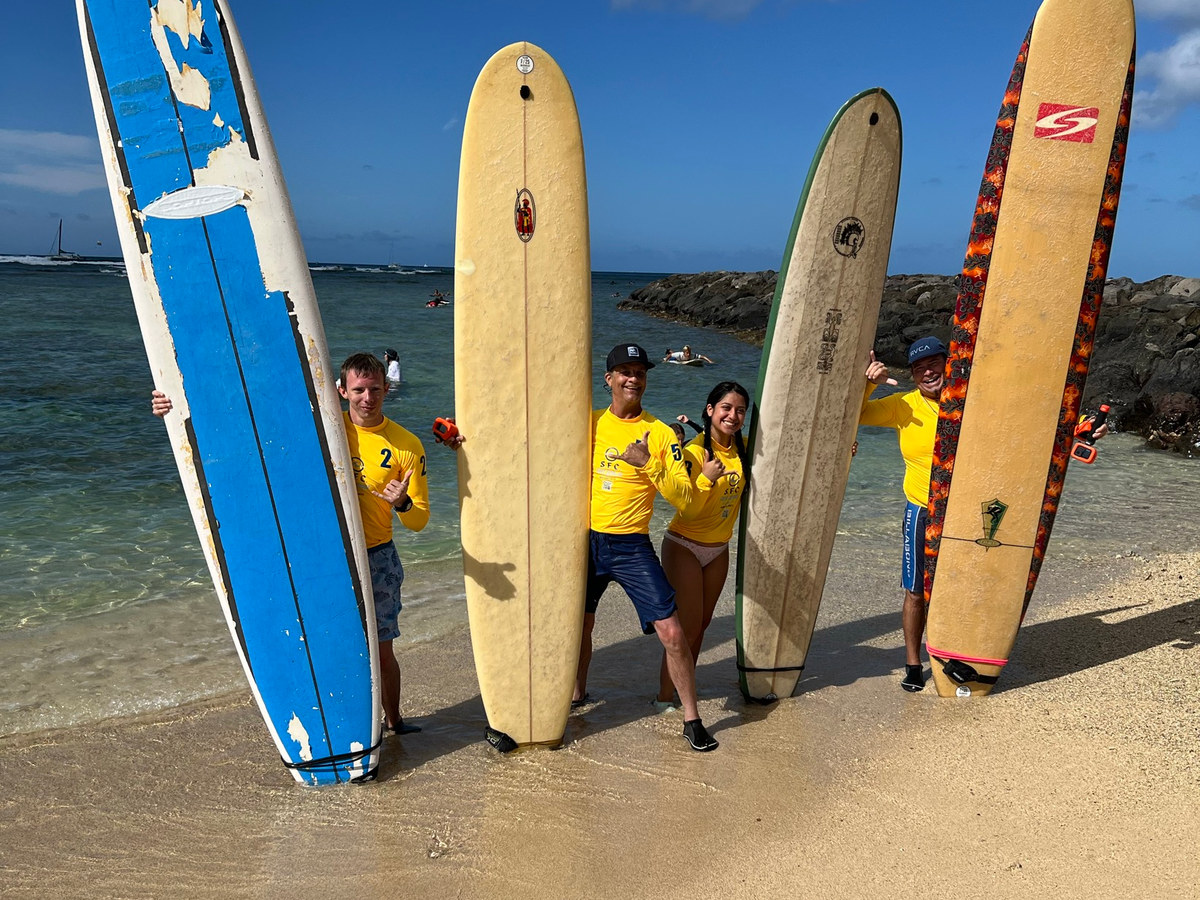 SFC surfers standing on the Waikīkī shoreline with lesson boards before paddling out